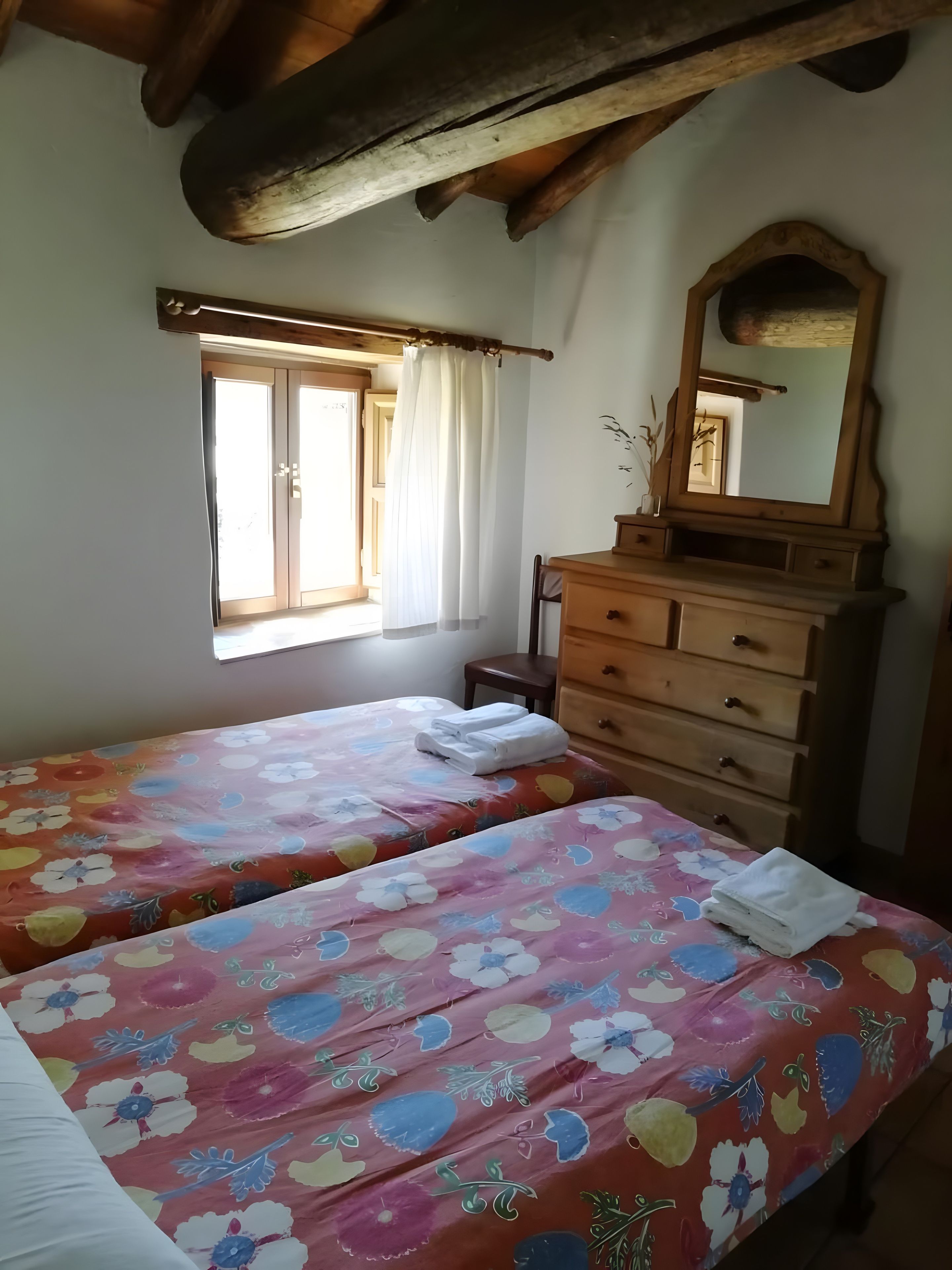 Een slaapkamer met twee bedden, een houten dressoir, een raam met gordijnen en een spiegel.