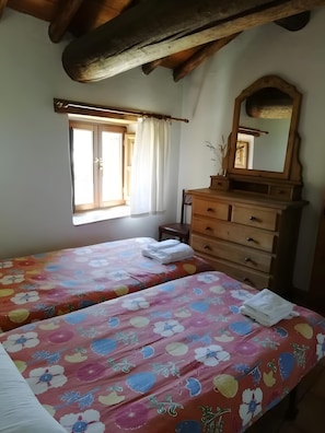 Een slaapkamer met twee bedden, een houten dressoir, een raam met gordijnen en een spiegel.