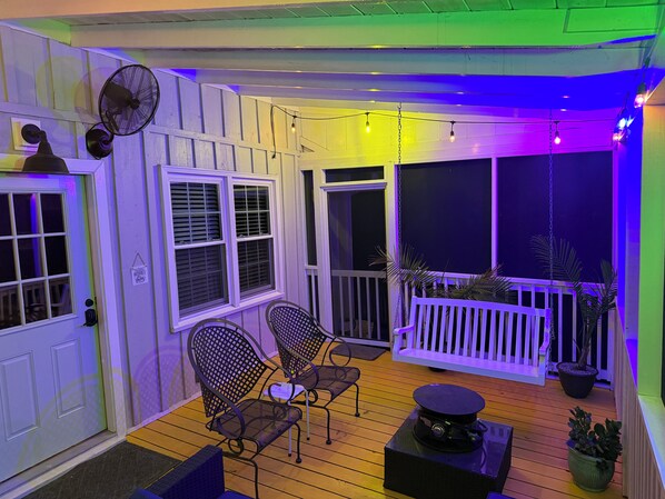 A covered porch with two chairs, a table, and a fan.