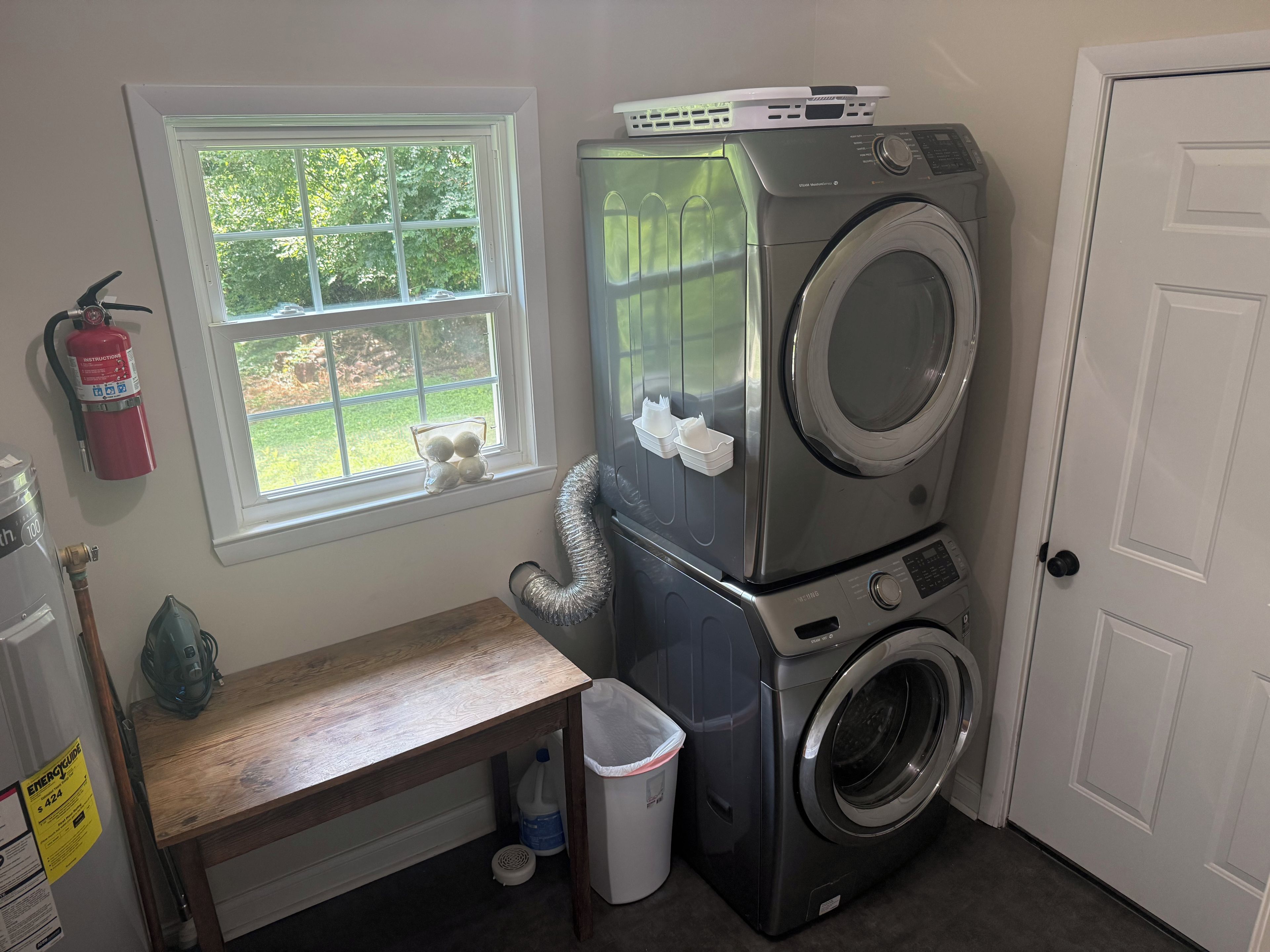 A laundry room with stacked washers and dryers, a window with a view, a fire extinguisher, and a bench.