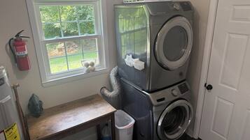 A laundry room with stacked washers and dryers, a window with a view, a fire extinguisher, and a bench.