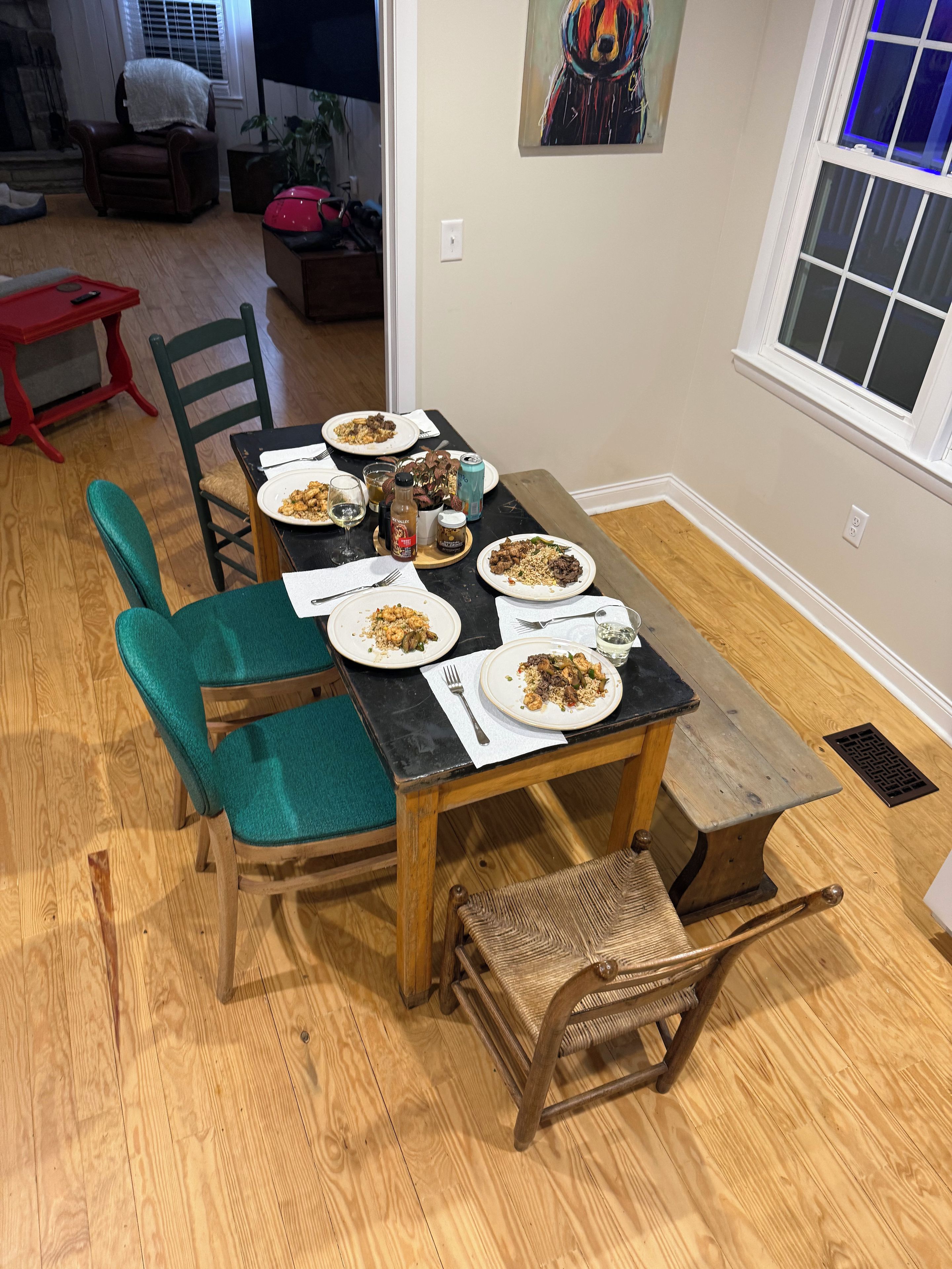 A dining area with a wooden table set for four, surrounded by chairs with green cushions.