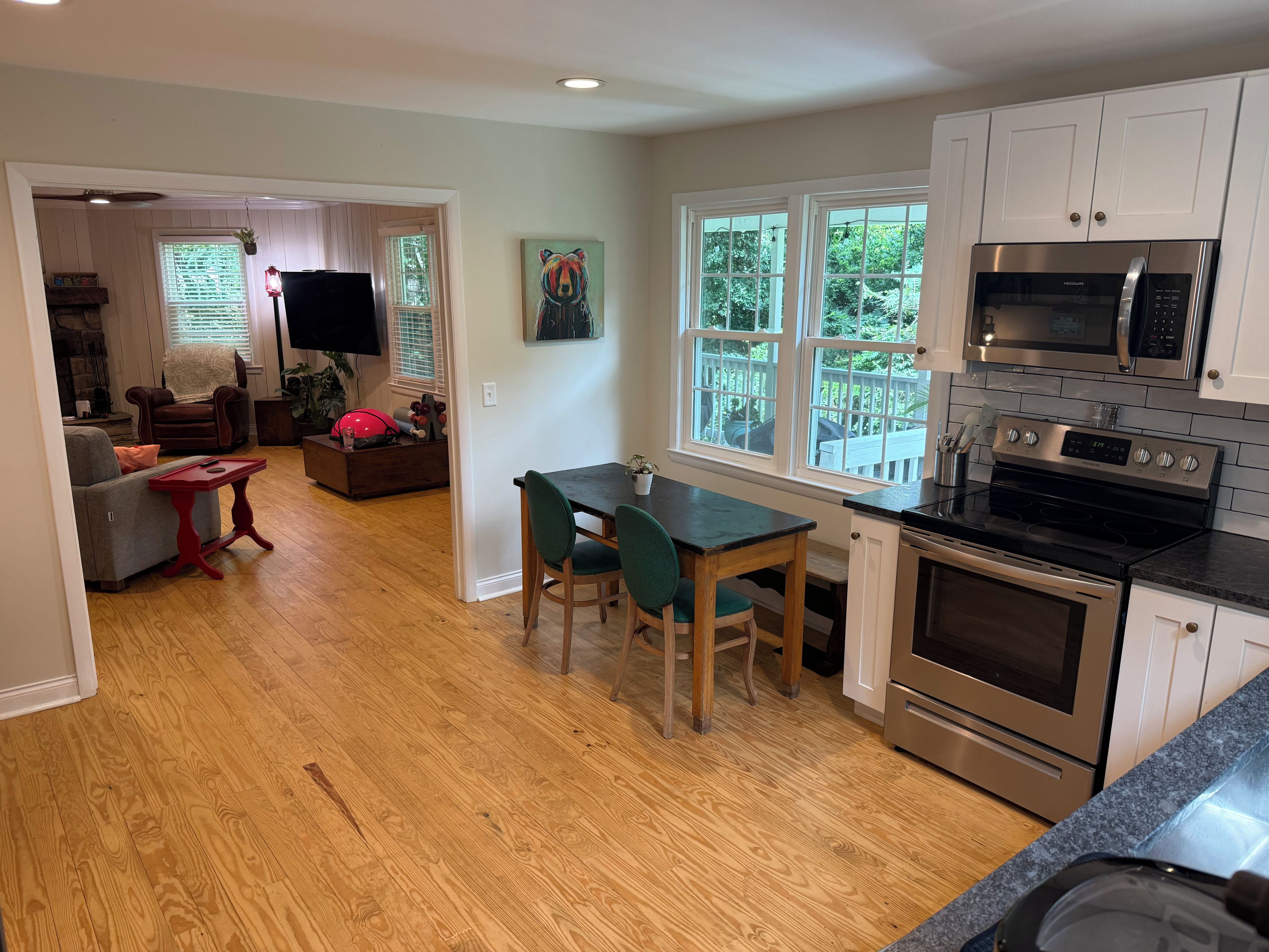 A modern kitchen with stainless steel appliances, a dining area with a table and chairs, and a living room with a sofa and a TV.