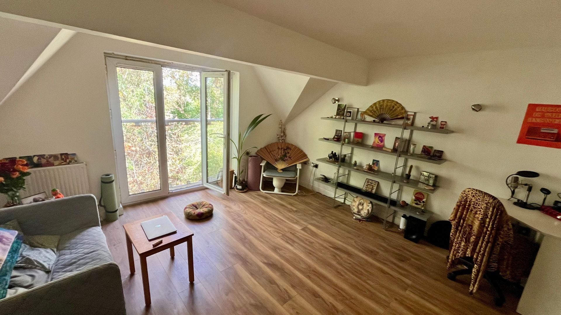 A living room with a sofa, a table, a fan, and a bookshelf.