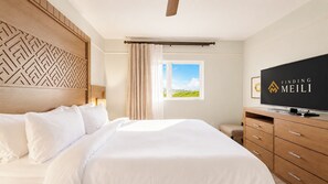 Quarto de hotel com uma cama grande, televisão, cabeceira de madeira, janela com vista e ventilador de teto.