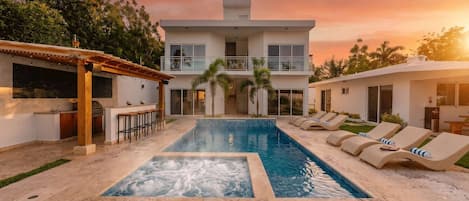 A two-story house with a swimming pool, outdoor bar, and lounge chairs.
