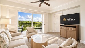 Quarto de hotel com varanda, televisão e área de estar com sofá e cadeiras.