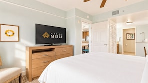 Quarto de hotel com cama, televisão, cómoda de madeira, cadeira e porta para o banheiro.