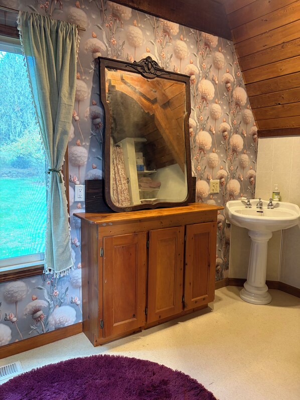 A bathroom with a wooden cabinet, a mirror, a sink, and floral wallpaper. - Amazing 3-bedroom bed & breakfast in charming Foster (Foster)