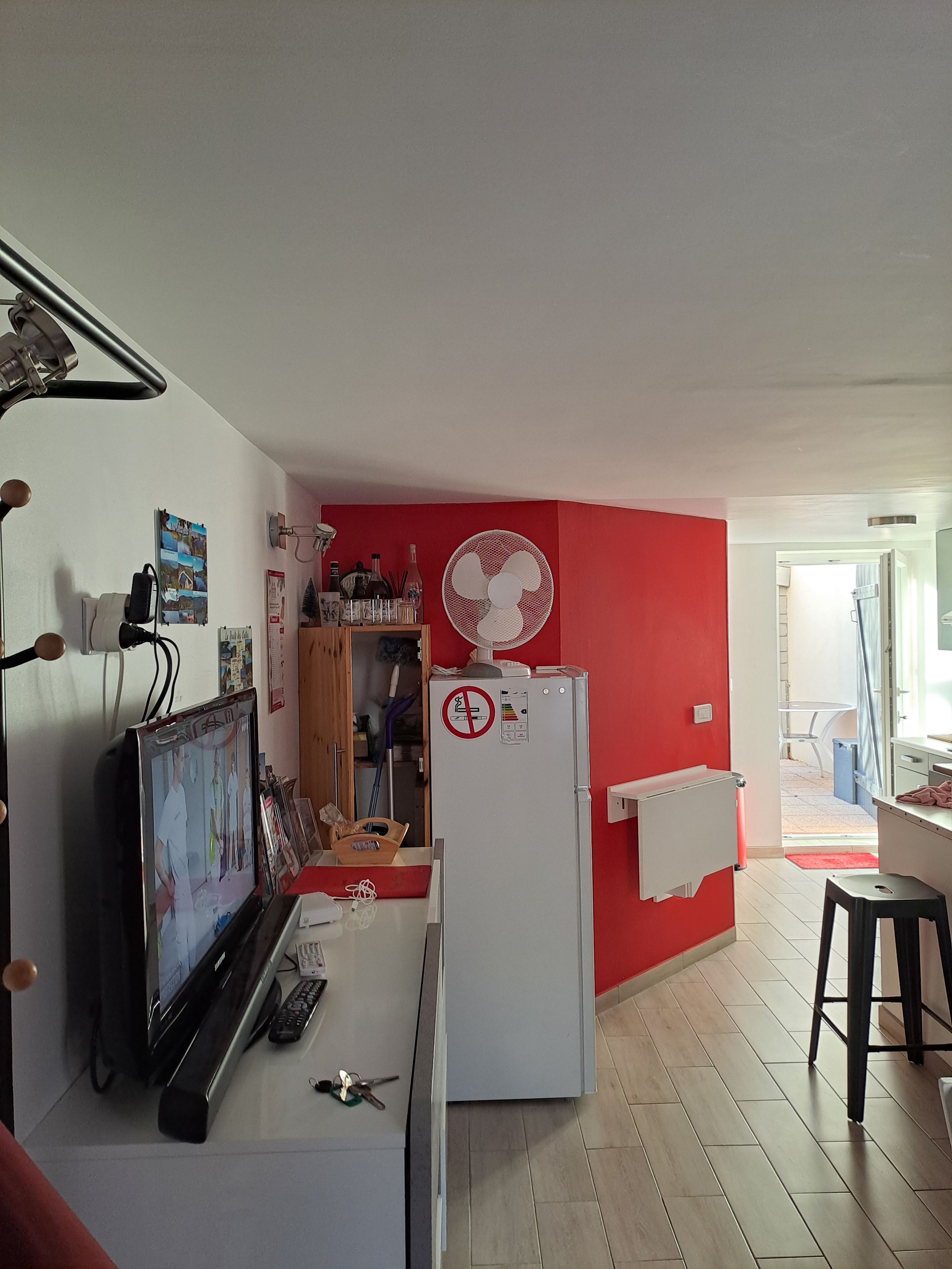 Une cuisine compacte équipée d’un réfrigérateur, d’un ventilateur, d’une télévision et d’un coin repas avec une table et des chaises.