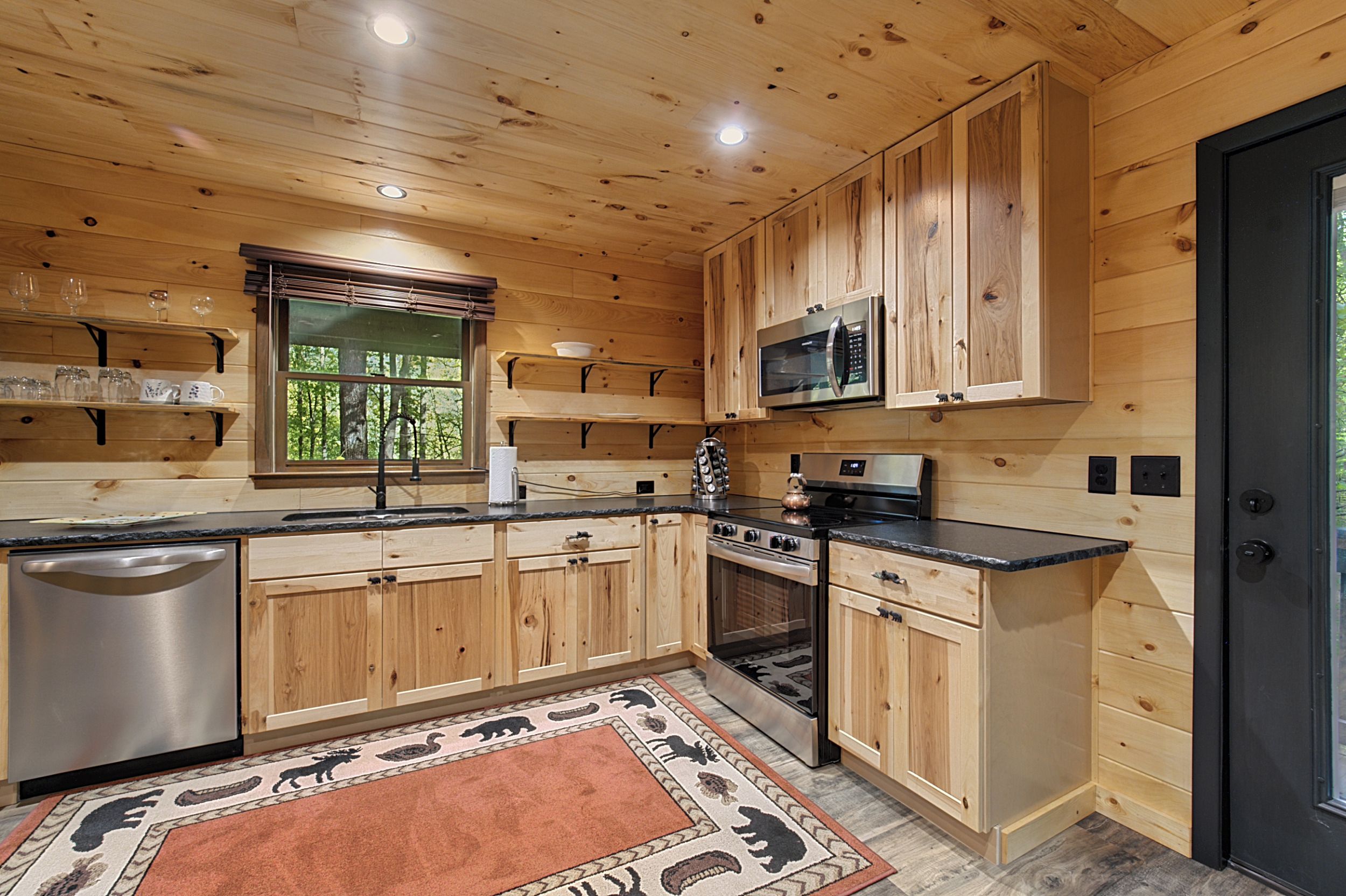 A wooden cabin interior with a kitchen featuring a stainless steel refrigerator, a microwave, and an oven.