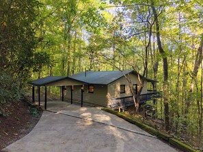 A cabin with a covered porch, a fenced deck, and a concrete driveway surrounded by trees. - Lovely 2-bedroom cabin in the Smoky Mountains in a gated community (Franklin)