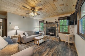 A cozy living room with a fireplace, wooden ceiling, and large windows. - Lovely 2-bedroom cabin in the Smoky Mountains in a gated community (Franklin)