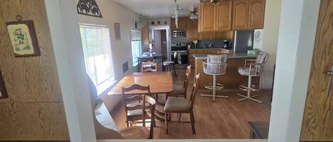 A dining area with a wooden table and chairs, a kitchen with wooden cabinets, and a bar area with stools.