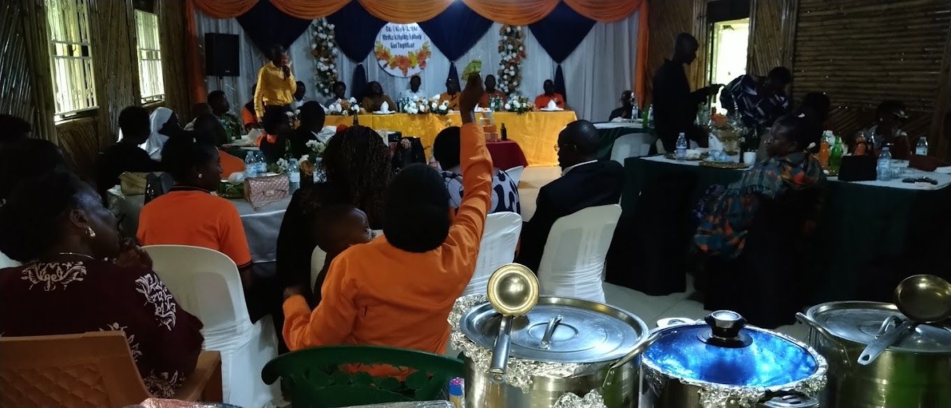 A formal event with attendees seated at round tables, a stage with a speaker, and a buffet setup.