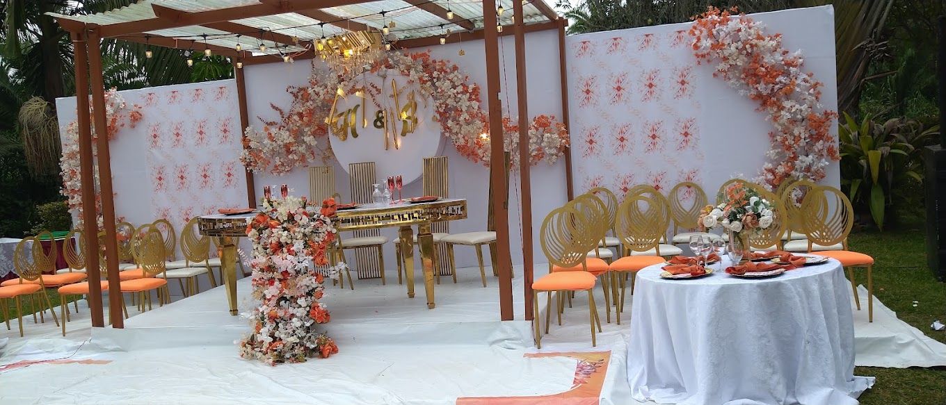An outdoor wedding setup with a white tablecloth, orange chairs, and floral decorations.