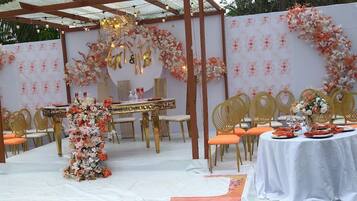 An outdoor wedding setup with a white tablecloth, orange chairs, and floral decorations.