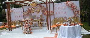 An outdoor wedding setup with a white tablecloth, orange chairs, and floral decorations.