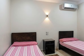A bedroom with two beds, a nightstand, a wall-mounted air conditioner, and a light fixture. - El Eman Hotel (Ar Radiseyah Bahri Edfu)
