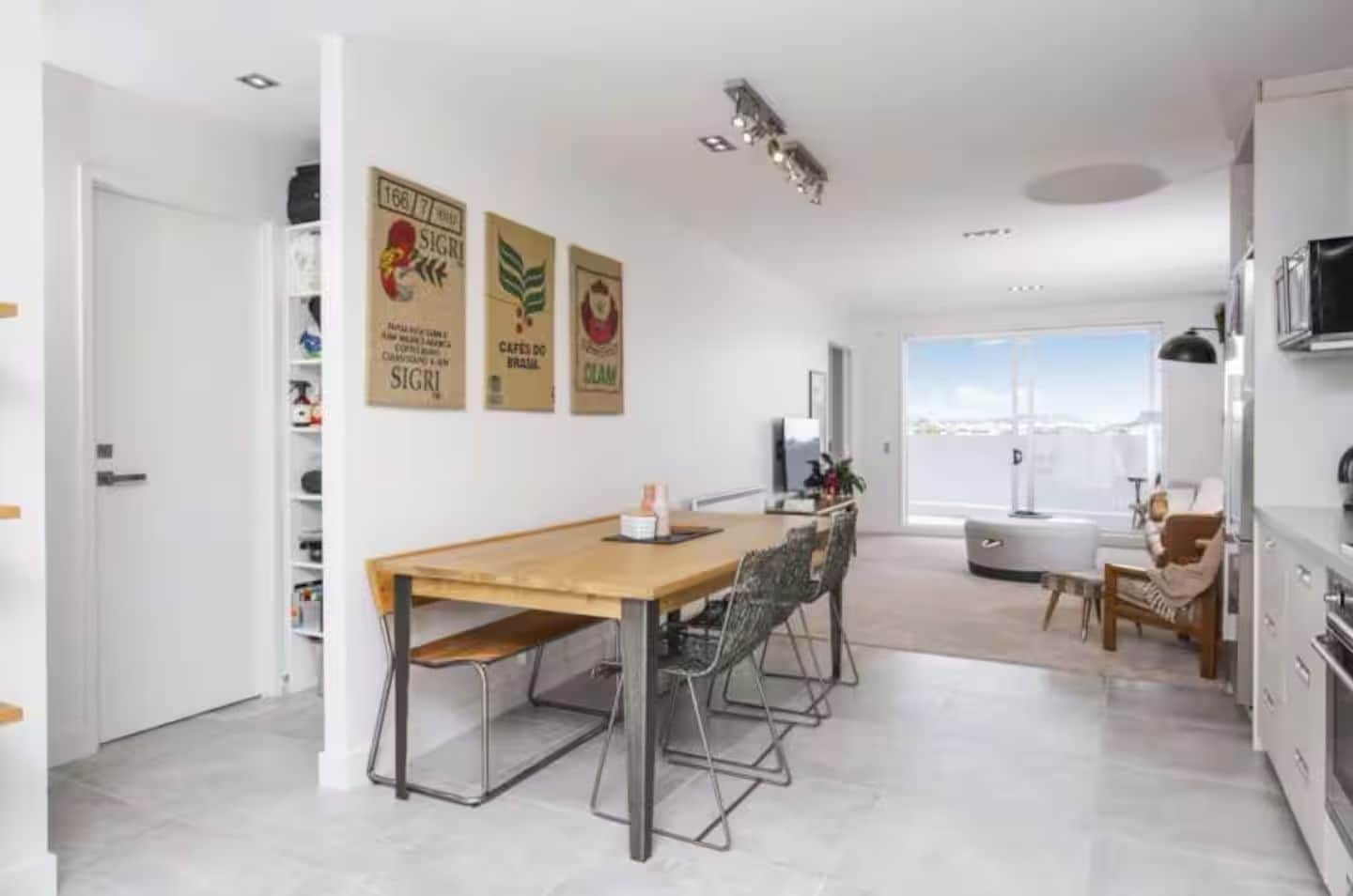 A modern kitchen with a dining area, white walls, and a large window.