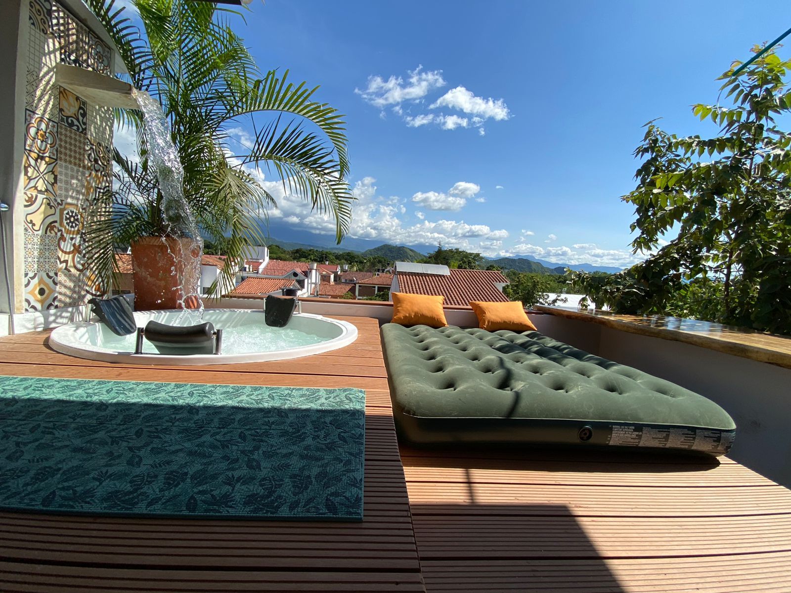 A rooftop lounge with a hot tub, a cushioned seating area, and a view of the surrounding buildings and landscape.