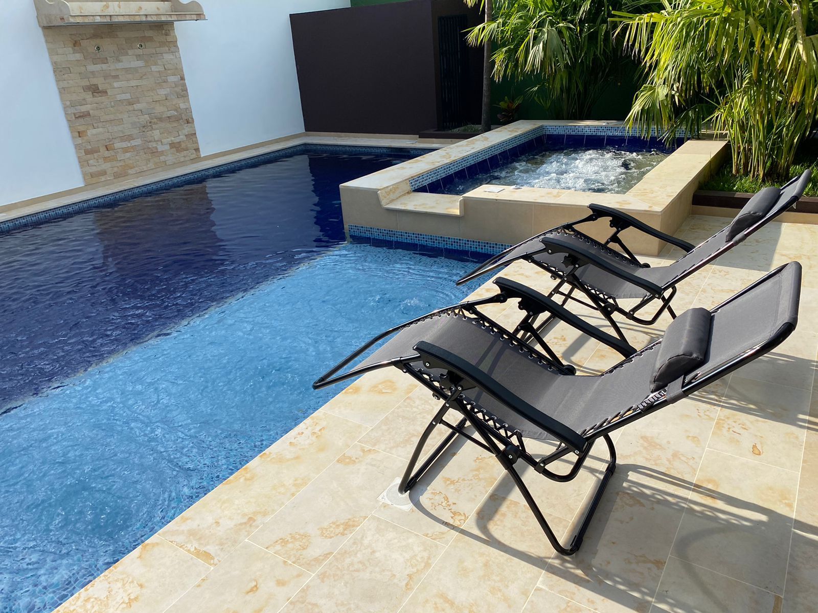 A swimming pool with two lounge chairs and a small hot tub area.
