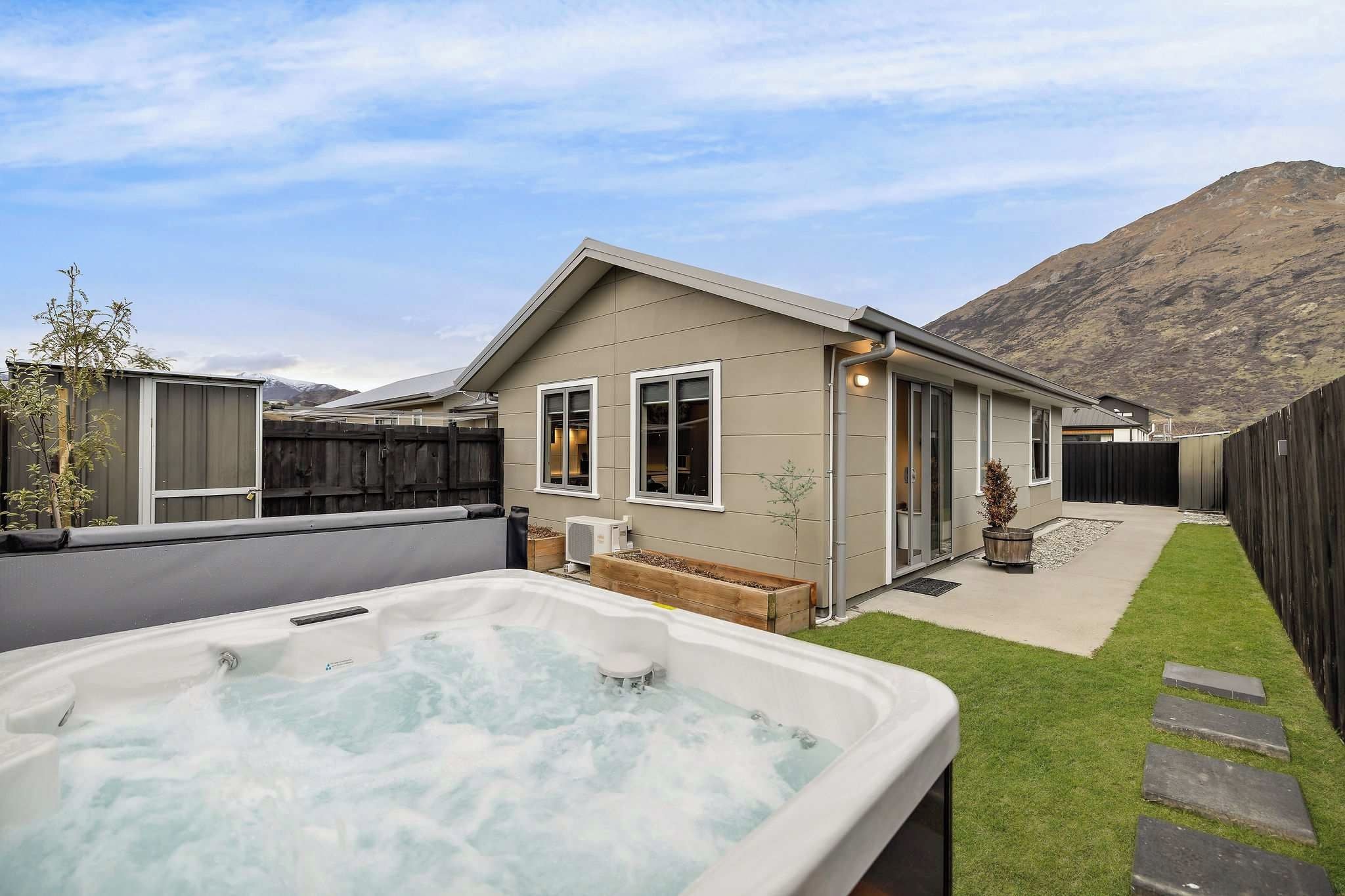 A modern house with a hot tub in the backyard, a wooden fence, and a mountain in the background.