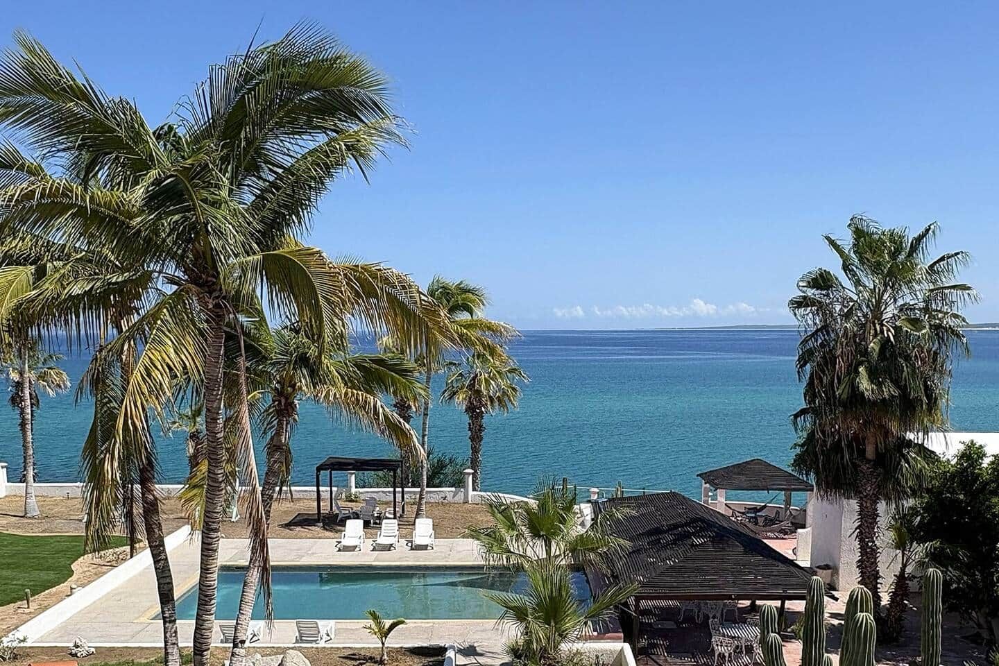 A pool area with lounge chairs and a view of the ocean.