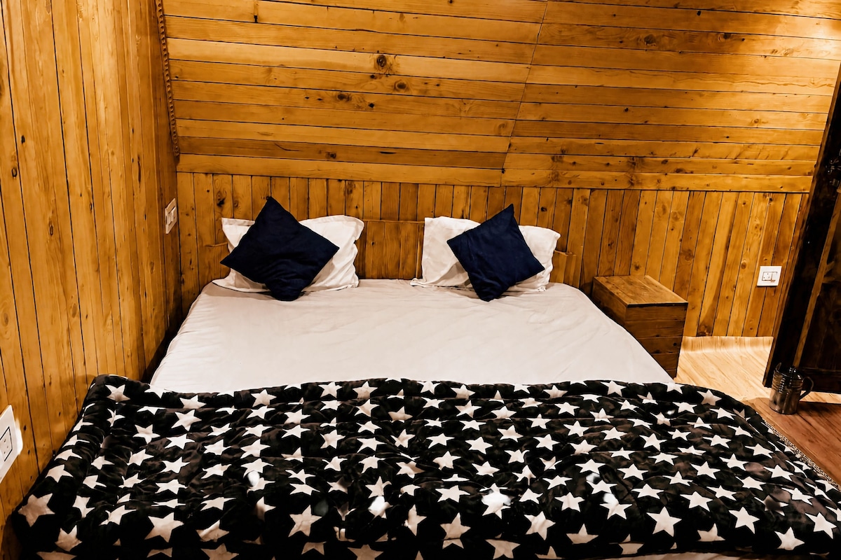 Una habitación con paneles de madera, una cama, dos almohadas, una mesita de noche y una manta con motivos de estrellas.