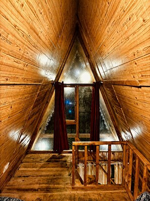 Un ático triangular con paredes de madera, una ventana con cortinas y un banco de madera.