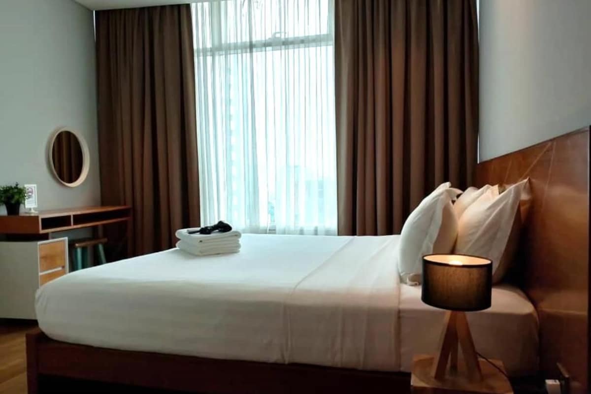 Habitación de hotel con cama, lámpara de noche y vista a la ciudad a través de amplias ventanas.