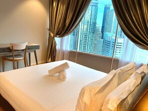 Habitación de hotel con cama, escritorio y silla. La habitación tiene vista a edificios altos.