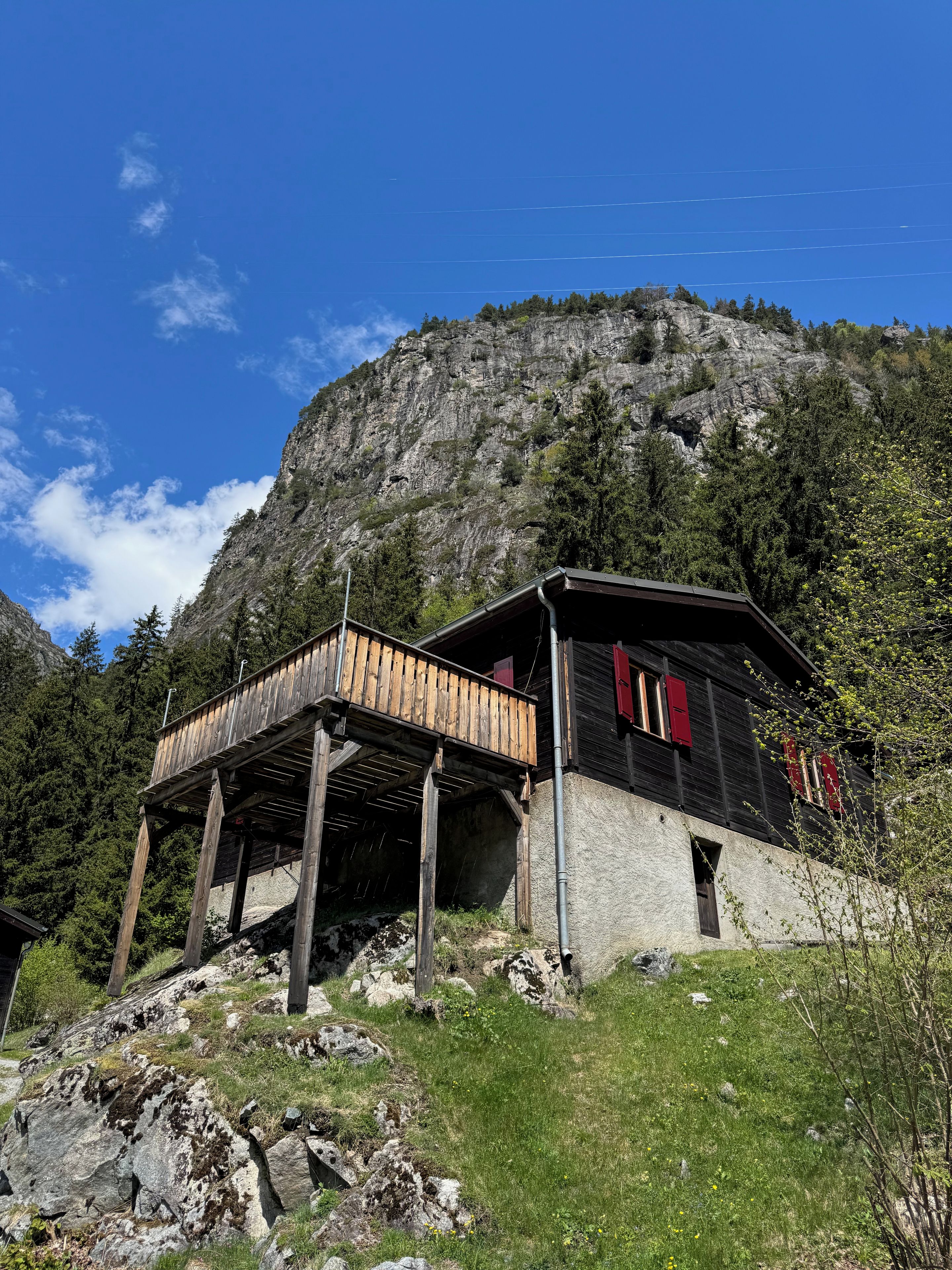 A rustic cabin with a wooden deck, set against a mountainous backdrop.