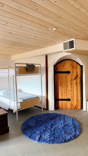 Une pièce avec des lits superposés, une porte en bois et un tapis bleu.
