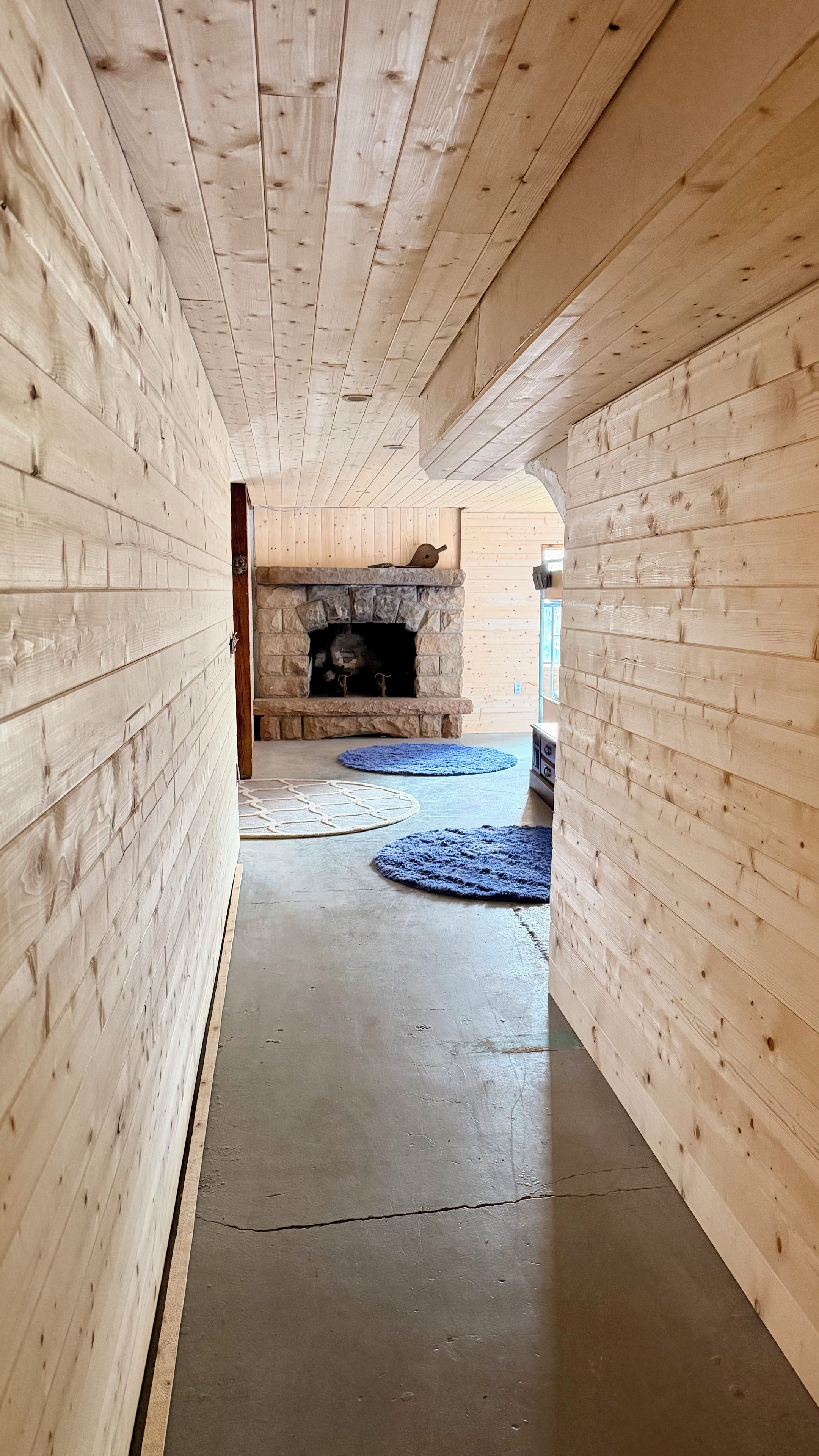 A corridor with wooden walls, a stone fireplace, and two blue rugs on the floor.