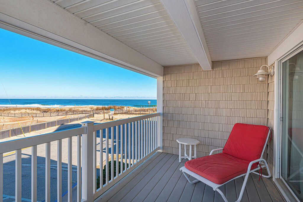 A balcony with a view of the beach, a red lounge chair, and a small table.