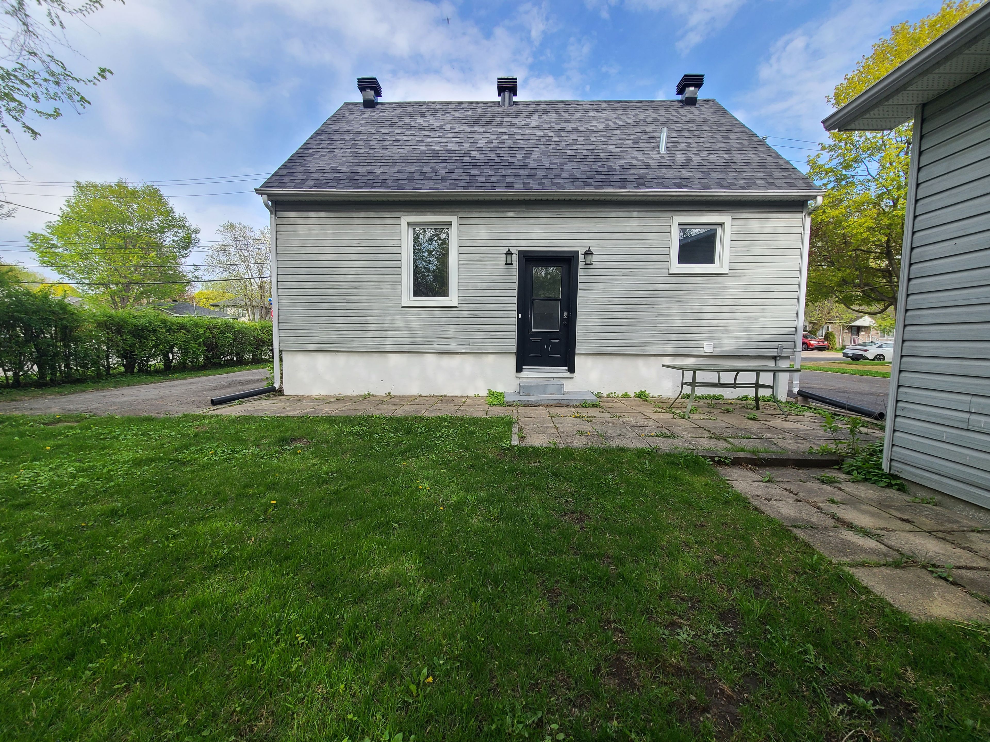 Ein eingeschossiges Haus mit einer schwarzen Haustür, einer kleinen Veranda und einem Rasen.