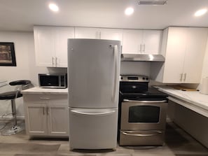 Una cocina moderna con armarios blancos, un refrigerador de acero inoxidable, un microondas, un horno y una estufa a gas.
