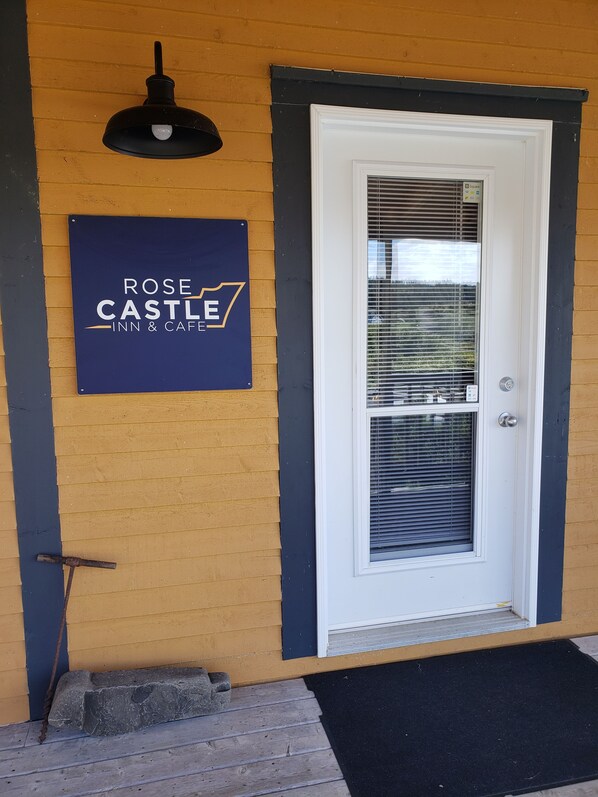 L’entrée d’un hôtel, avec une enseigne indiquant « ROSE CASTLE INN & CAFE », une porte dotée d’une fenêtre et un luminaire noir fixé au mur.