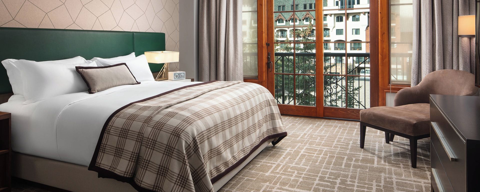 A hotel room with a bed, a chair, a nightstand, and a view of the outside.