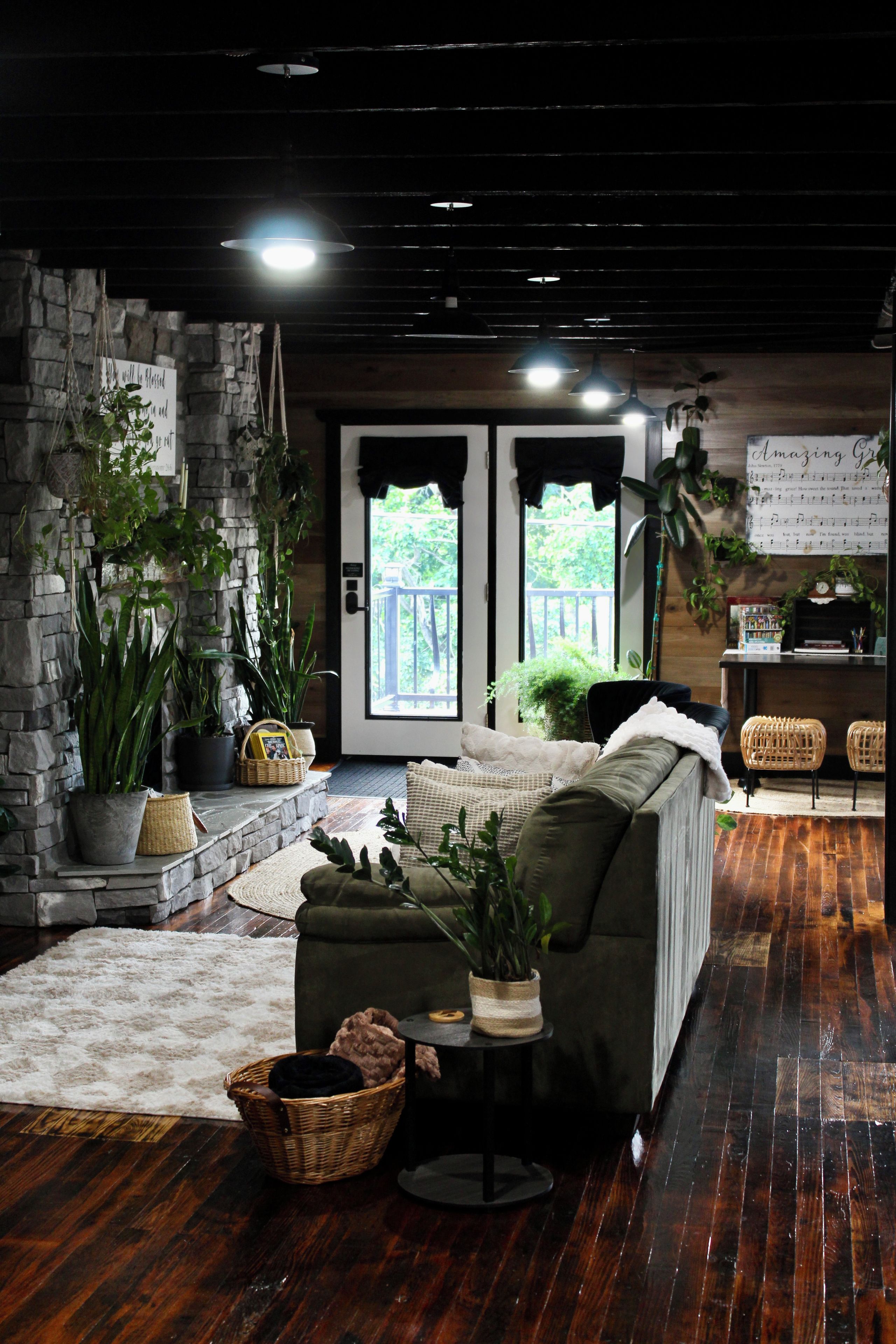 A cozy living room with a stone wall, a sofa, a coffee table, and various plants.