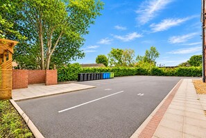 Ein Parkplatz mit markierten Stellplätzen, einer Backsteinmauer und einer Reihe von Mülltonnen.