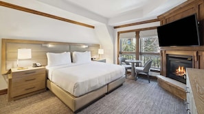 Una habitación de hotel con cama, mesitas de noche, un escritorio con silla, chimenea y televisor.