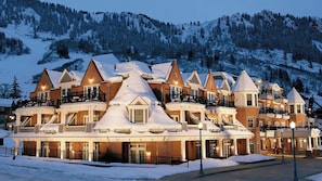 Ett hotell med flera våningar, vars fasad är täckt av snö, och som har balkonger samt en bergig bakgrund.