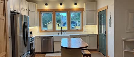 A modern kitchen with stainless steel appliances, wooden cabinets, a central island, and a view of the outside.