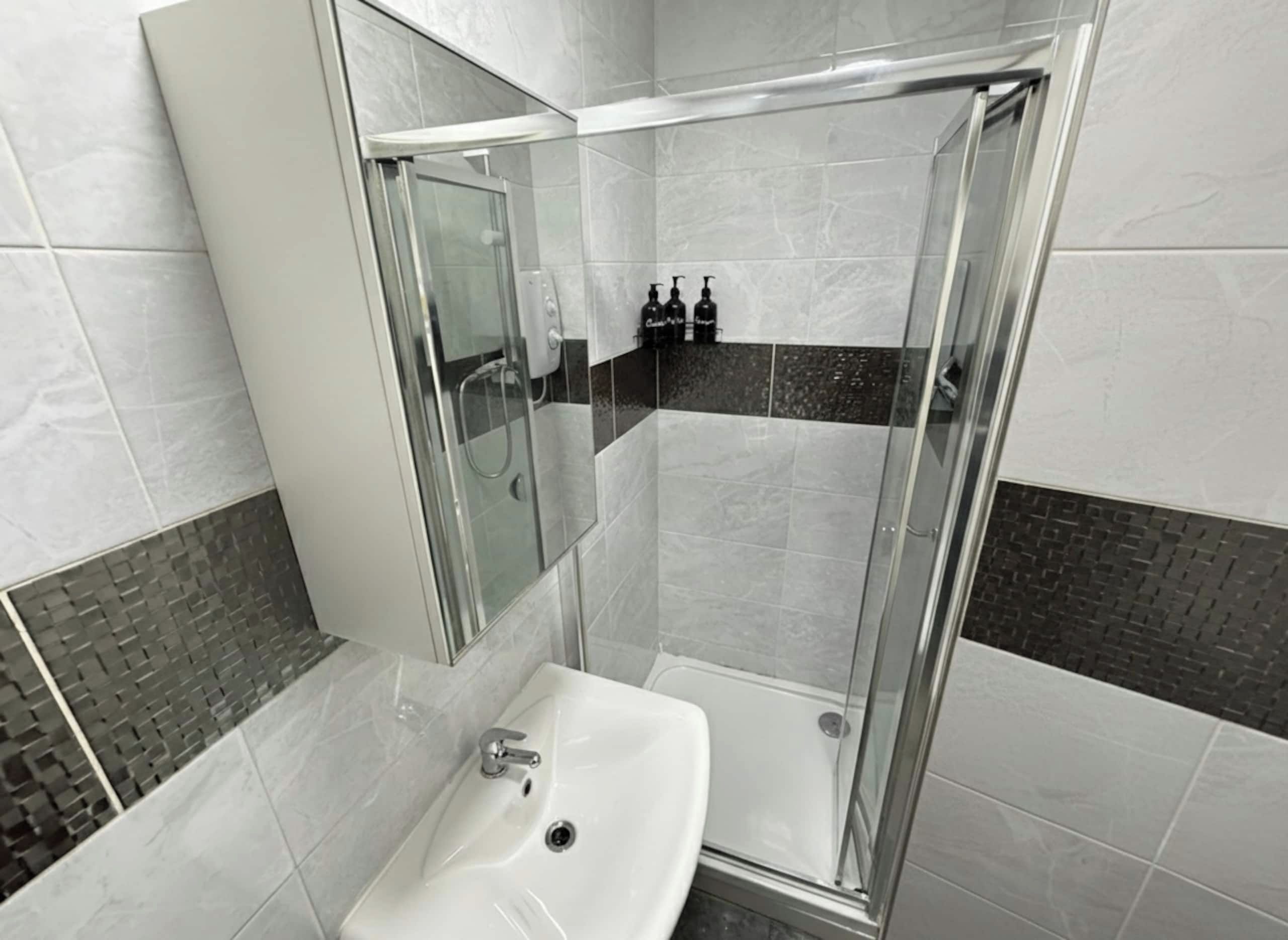Un baño moderno con ducha de vidrio, un lavabo blanco y un espejo.