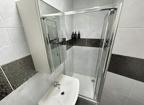 Un baño moderno con ducha de vidrio, un lavabo blanco y un espejo.