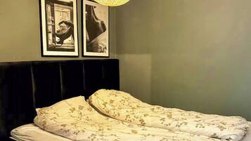 A bedroom with a bed, a bedside table, a lamp, and two framed pictures on the wall.