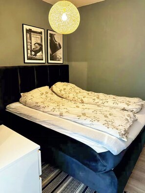 A bedroom with a bed, a bedside table, a lamp, and two framed pictures on the wall. - Bright flat in Storo with balcony (Oslo)