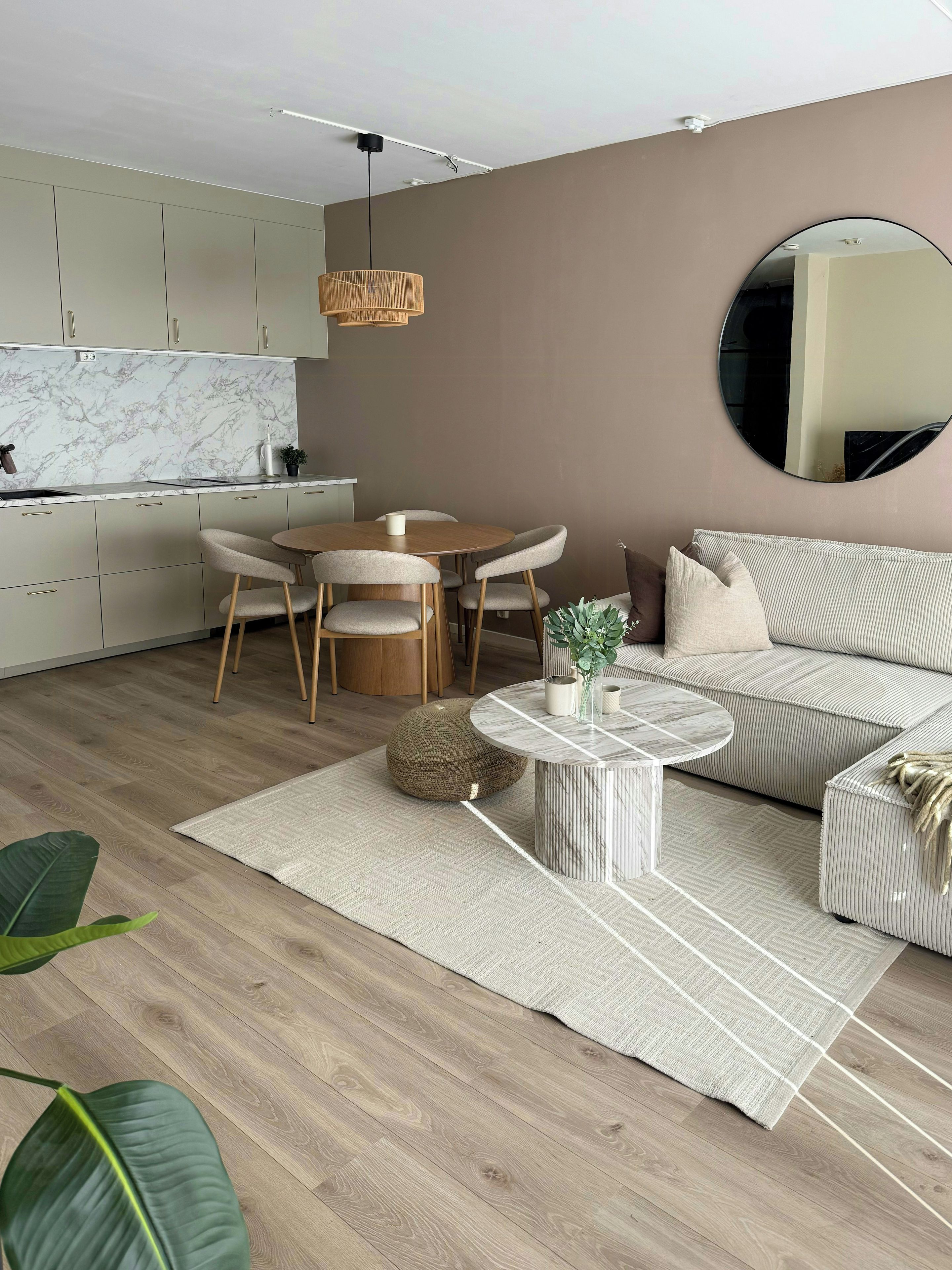 A modern living room with a round dining table, a sofa, a coffee table, and a kitchen in the background.